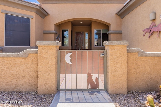 entrance to property featuring fence, stucco siding, and a gate