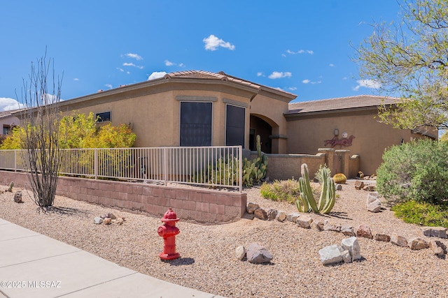 view of front of home with stucco siding, fence, and a tile roof