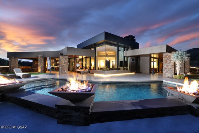 pool at dusk with a patio, an infinity pool, and a fire pit