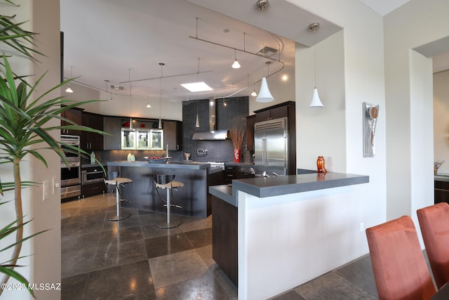 kitchen featuring dark countertops, wall chimney exhaust hood, tasteful backsplash, rail lighting, and stainless steel appliances