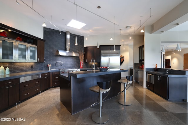 kitchen featuring appliances with stainless steel finishes, wall chimney range hood, dark countertops, and a kitchen bar