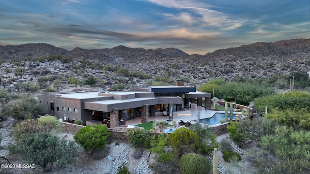 back of property at dusk with stucco siding, a patio area, a mountain view, and an outdoor pool