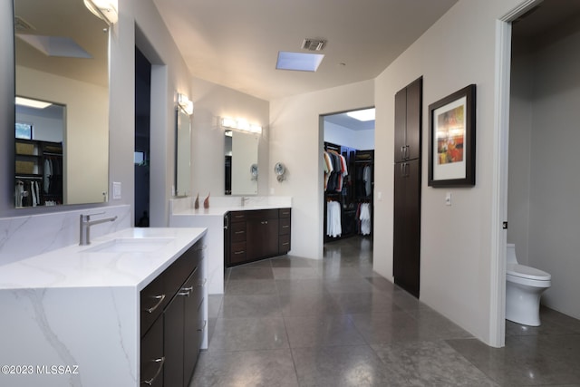 full bath featuring visible vents, two vanities, a sink, toilet, and a spacious closet