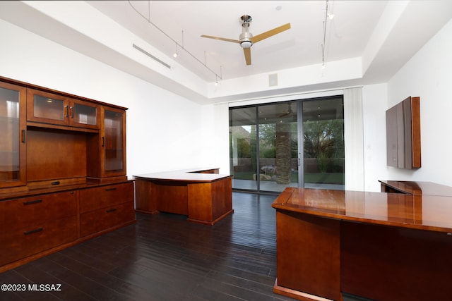 unfurnished office with a ceiling fan, a tray ceiling, dark wood-style floors, and rail lighting