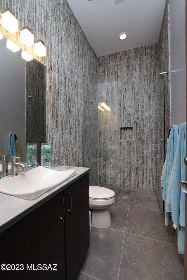 bathroom featuring vanity, a tile shower, toilet, and tile walls