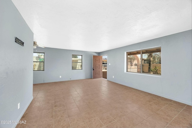 unfurnished room with baseboards, a ceiling fan, plenty of natural light, and a textured ceiling