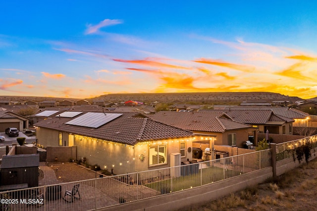 back of house at dusk featuring roof mounted solar panels, a patio area, stucco siding, and a fenced backyard