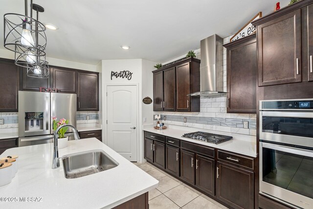 kitchen featuring decorative light fixtures, wall chimney exhaust hood, a sink, light countertops, and stainless steel appliances