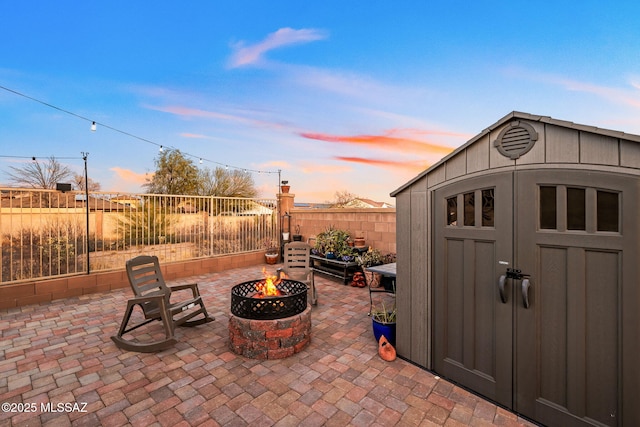 outdoor structure at dusk featuring a fenced backyard, an outdoor structure, a fire pit, and a shed