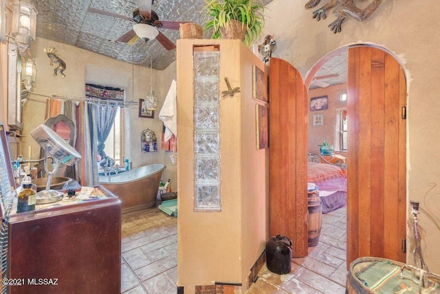 bathroom with a freestanding bath, stone tile flooring, and ceiling fan