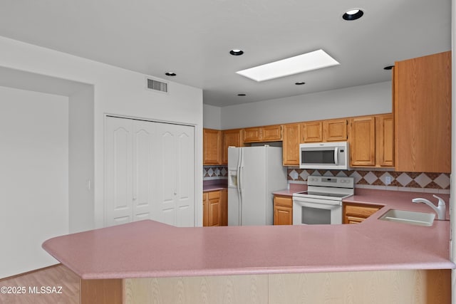 kitchen featuring visible vents, a sink, white appliances, backsplash, and a skylight