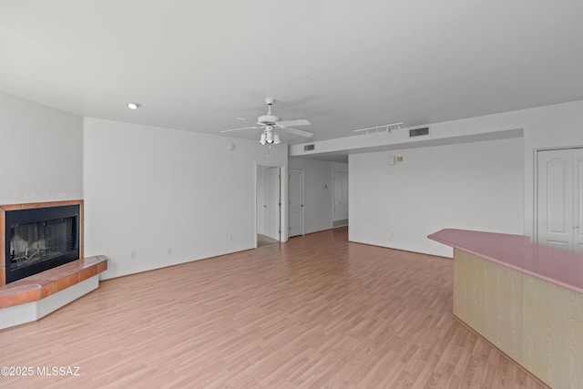 unfurnished living room with visible vents, ceiling fan, light wood-type flooring, and a tile fireplace