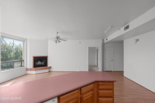 unfurnished living room featuring a tiled fireplace, light wood finished floors, visible vents, and a ceiling fan