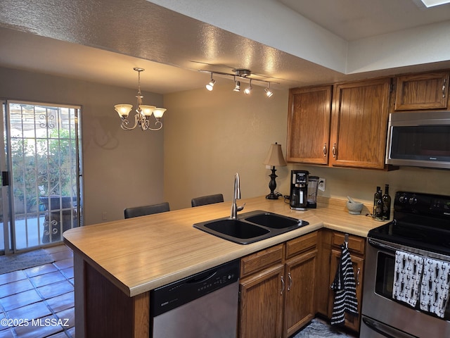 kitchen featuring an inviting chandelier, a peninsula, light countertops, appliances with stainless steel finishes, and a sink