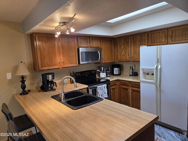 kitchen featuring white refrigerator with ice dispenser, stainless steel microwave, a sink, range with electric cooktop, and brown cabinets