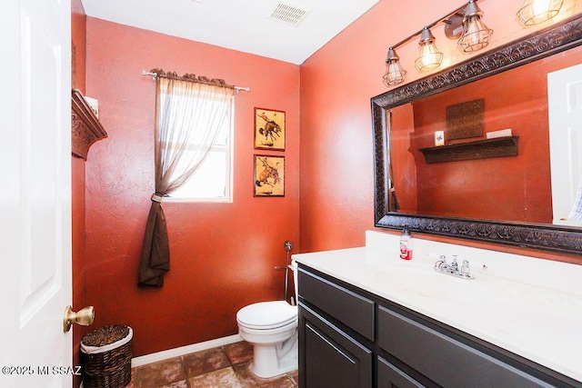 bathroom featuring toilet, vanity, visible vents, and baseboards