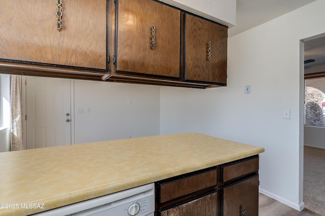 kitchen featuring baseboards, white dishwasher, light countertops, and dark brown cabinets