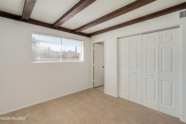 unfurnished bedroom featuring light carpet, a closet, baseboards, and beam ceiling