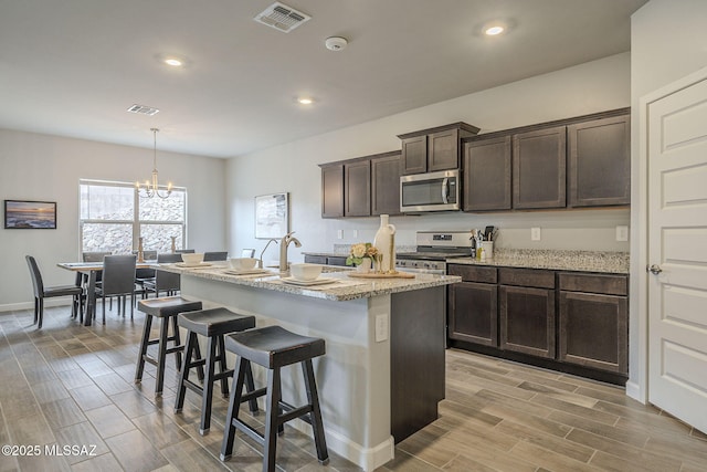 1117 W Valley Meadow Ln, Sahuarita, AZ 85629 - kitchen with stainless steel appliances, a kitchen breakfast bar, dark brown cabinets, a chandelier, and a kitchen island with sink