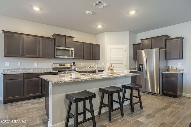 1117 W Valley Meadow Ln, Sahuarita, AZ 85629 - kitchen featuring stainless steel appliances, dark brown cabinets, wood finish floors, a breakfast bar, and baseboards