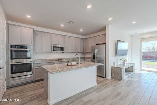 kitchen with a sink, appliances with stainless steel finishes, gray cabinets, and light wood-style floors