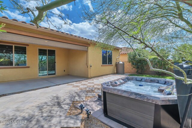 rear view of house with stucco siding, fence, a hot tub, and a patio area