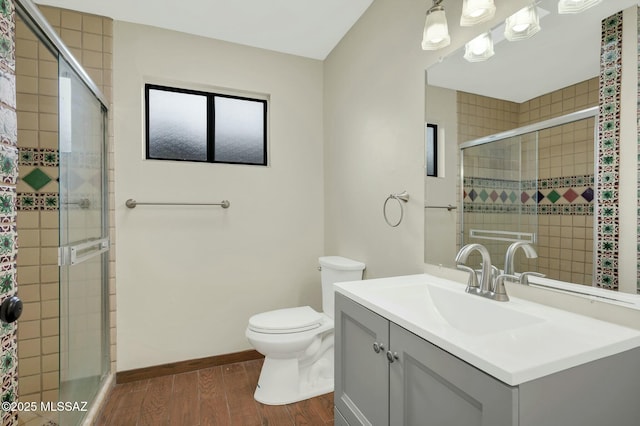 full bathroom with vanity, baseboards, toilet, a tile shower, and wood finished floors