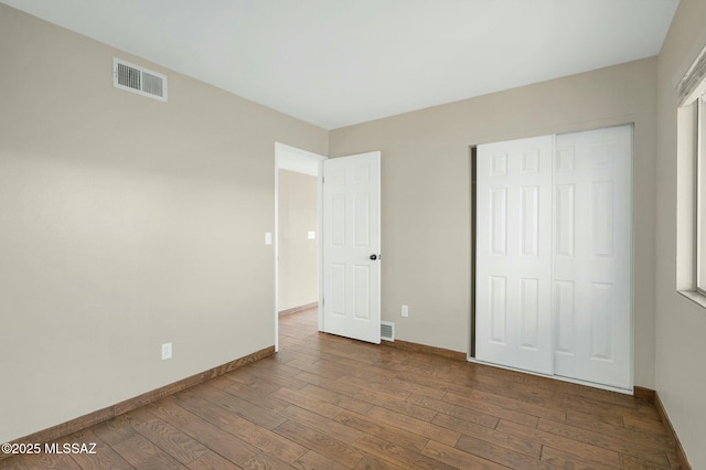 unfurnished bedroom featuring a closet, visible vents, hardwood / wood-style flooring, and baseboards