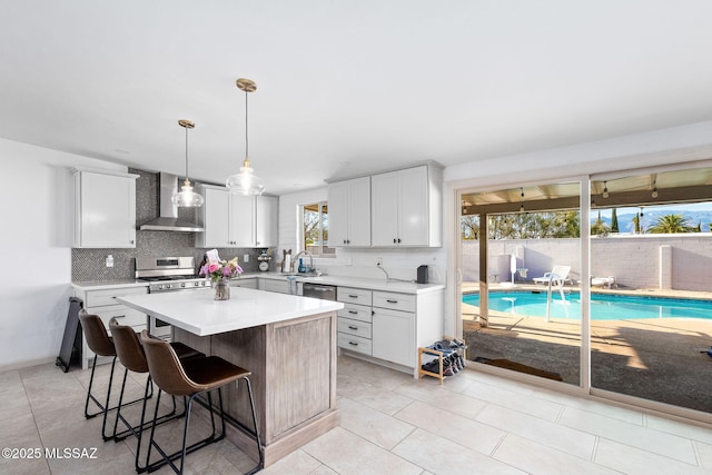 kitchen with gas range, wall chimney range hood, light countertops, a breakfast bar, and backsplash