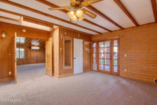 carpeted empty room with beam ceiling, a ceiling fan, brick wall, and wood walls