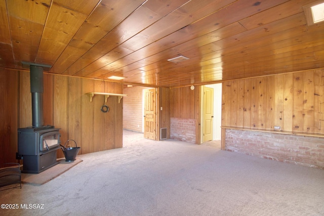 bonus room featuring brick wall, wooden walls, a wood stove, light colored carpet, and wooden ceiling