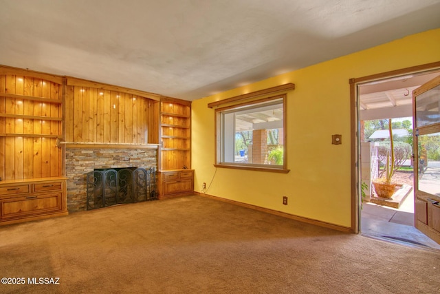 unfurnished living room with built in features, carpet flooring, baseboards, and a stone fireplace