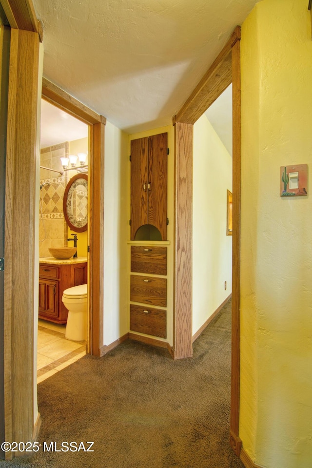 hall with a sink, baseboards, a textured wall, and carpet floors