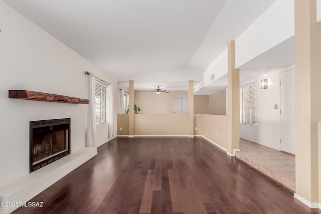 unfurnished living room with baseboards, vaulted ceiling, a ceiling fan, a fireplace with raised hearth, and wood finished floors