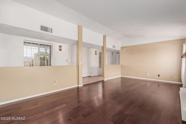 empty room featuring wood finished floors, baseboards, vaulted ceiling, and visible vents
