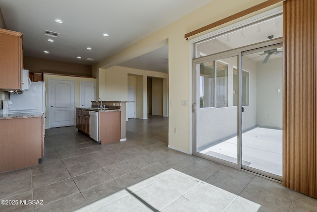 kitchen featuring white microwave, dishwasher, a sink, and light stone counters