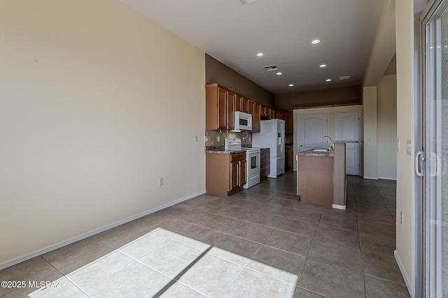 kitchen with white appliances, a sink, dark tile patterned floors, decorative backsplash, and baseboards