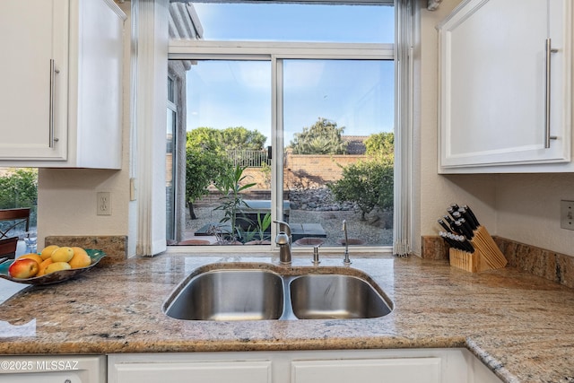 kitchen featuring a sink, white cabinetry, light stone counters, and a textured wall