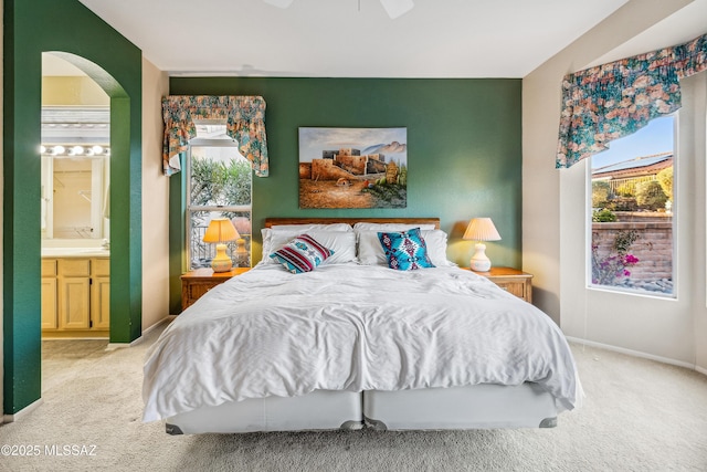 bedroom featuring light carpet, arched walkways, ensuite bath, and multiple windows