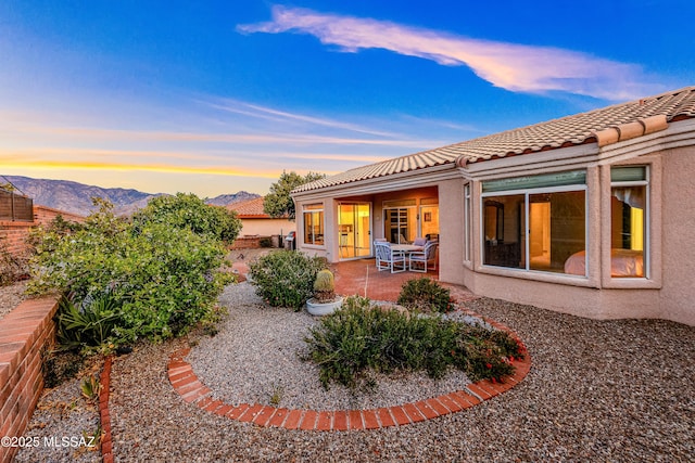 back of house at dusk with a patio, a mountain view, stucco siding, and a tile roof