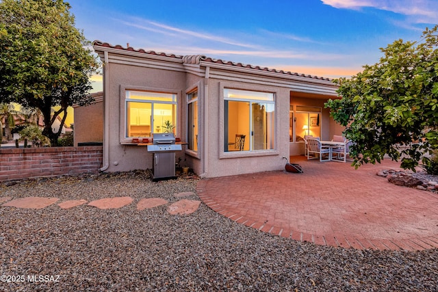 back of property at dusk with a tiled roof, a patio, and stucco siding
