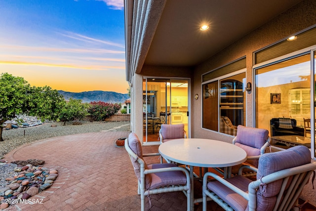 patio terrace at dusk featuring a mountain view and outdoor dining area
