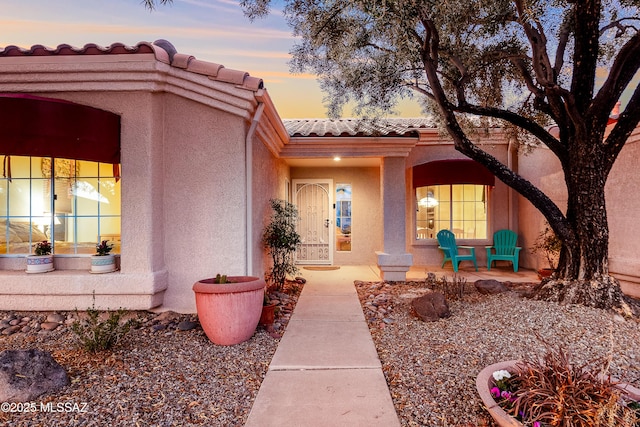 exterior entry at dusk with a tiled roof and stucco siding