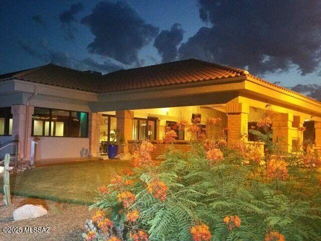 back of house at twilight featuring a tile roof