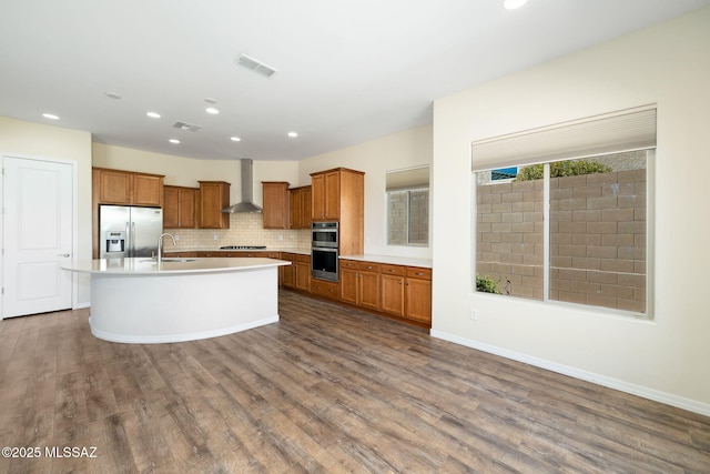 13906 N Rim Trl, Marana, AZ 85658 - kitchen featuring stainless steel appliances, brown cabinetry, dark wood-style floors, wall chimney range hood, and backsplash
