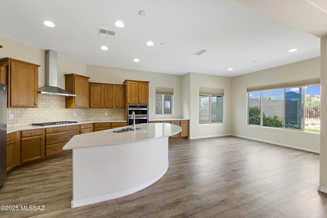 13906 N Rim Trl, Marana, AZ 85658 - kitchen with wall chimney range hood, stainless steel gas stovetop, brown cabinetry, a sink, and light countertops