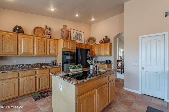 kitchen with arched walkways, black appliances, dark stone counters, and a kitchen island