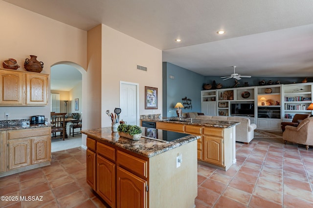 kitchen with visible vents, a center island, arched walkways, black electric stovetop, and dark stone counters
