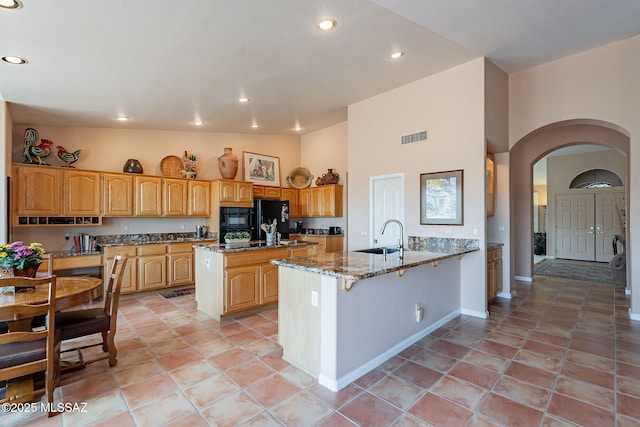 kitchen with visible vents, arched walkways, a sink, a peninsula, and stone counters