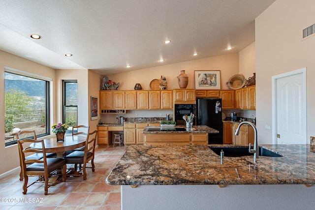 kitchen with dark stone counters, vaulted ceiling, black appliances, a center island, and a sink